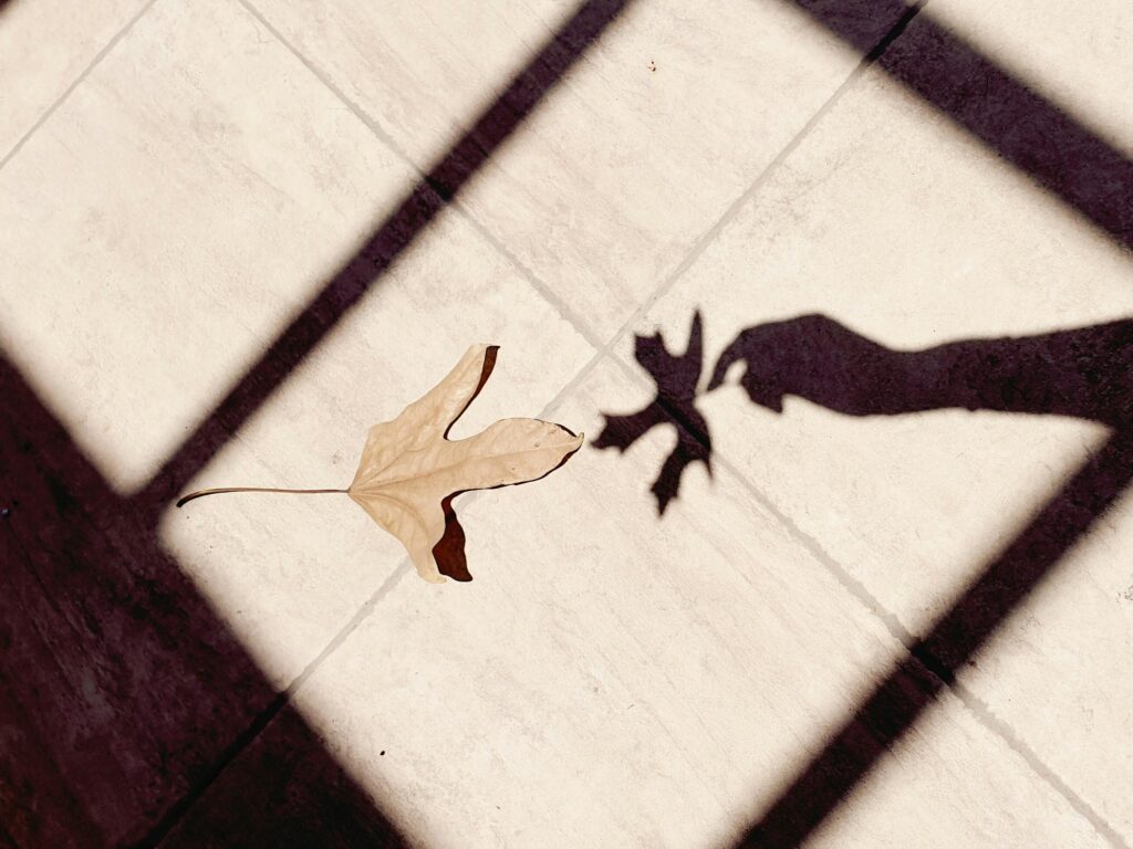 Creative shadow of a hand capturing a fall leaf on a tiled surface, evoking a sense of autumn.